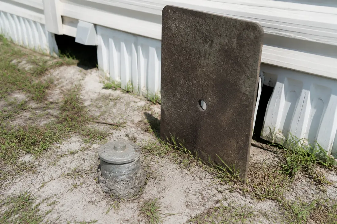 The head of a ground anchor at soil level with a stabilizer plate beside it