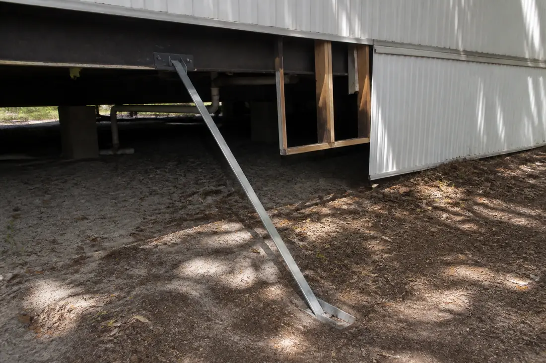 A steel tie-down strap running from the chassis of a manufactured home to a ground anchor