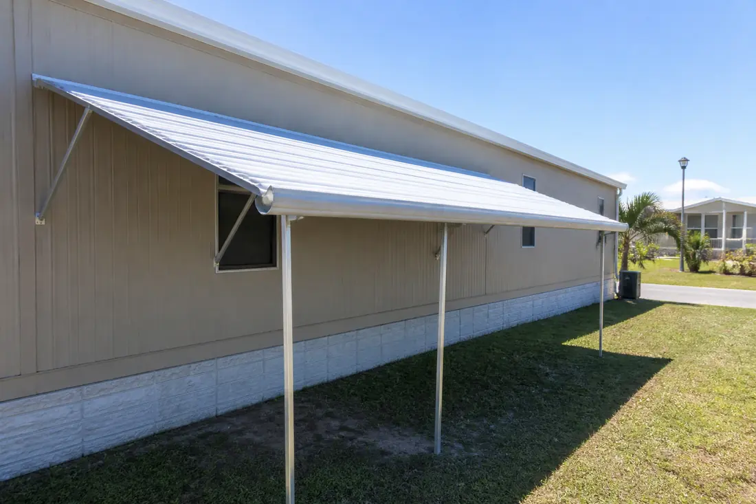 A window awning on the long side of a manufactured home with support arms bolted to the wall