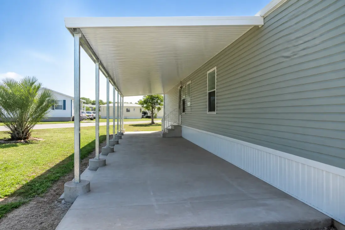 A freestanding carport beside a manufactured home, standing on its own posts at the outside edge